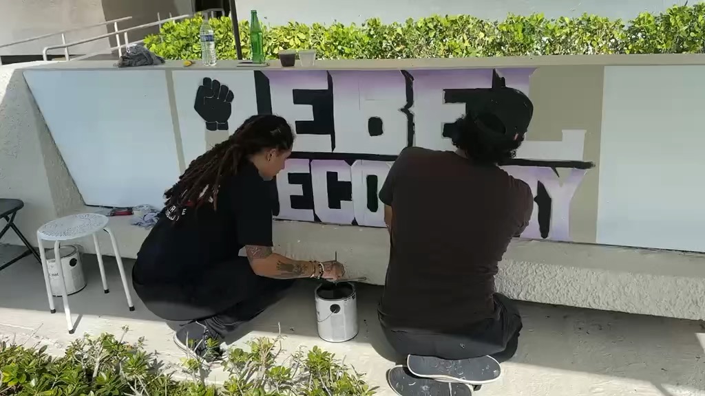 Two volunteers kneeling to paint the letters on the sign