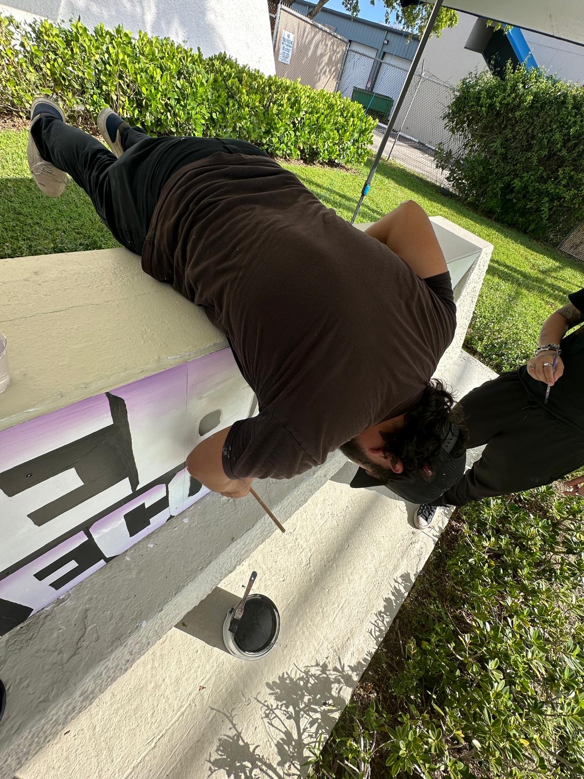 A volunteer leaning over the top of the sign to paint it