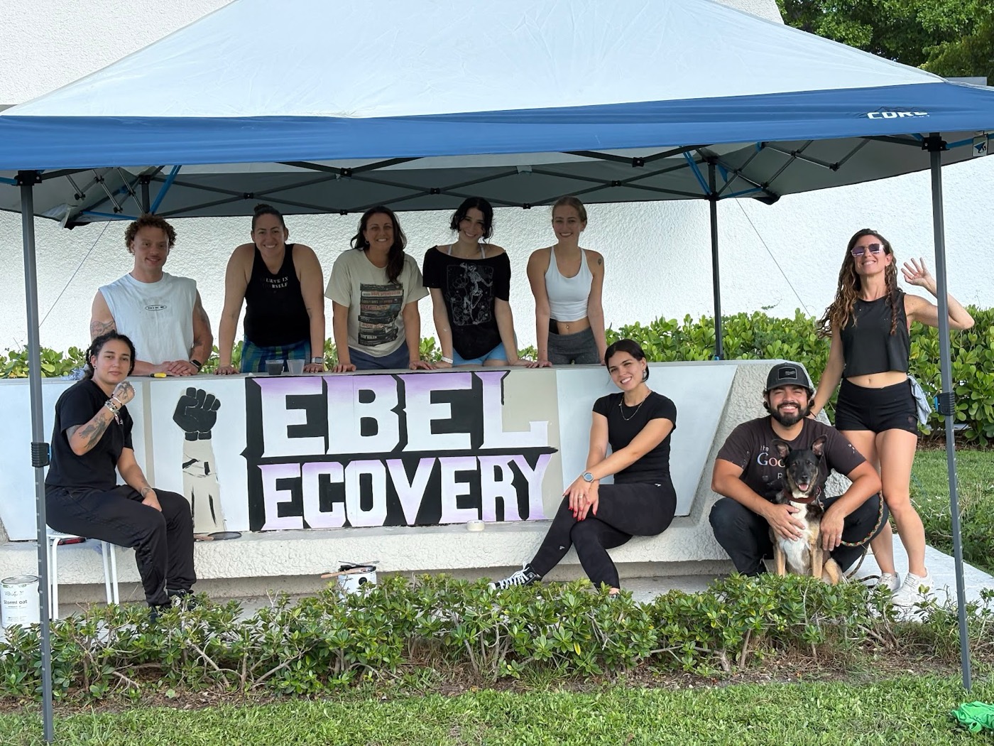 The volunteer team gathered at the Rebel Recovery sign they repainted